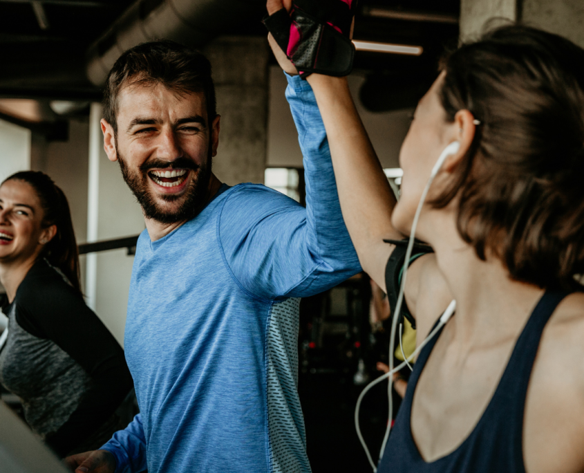 Two young people on the treadmill in a gym smiling and high fiving each other